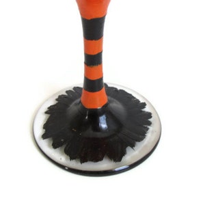 May include: A black and orange striped glass stem with a black base. The base has a black and white design that resembles a witch's hat.