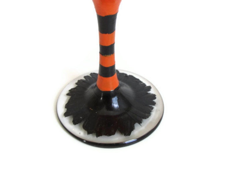May include: A black and orange striped glass stem with a black base. The base has a black and white design that resembles a witch's hat.