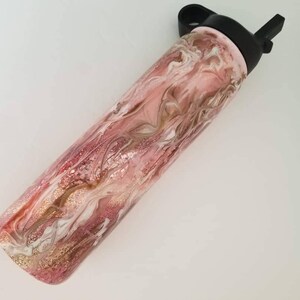 May include: A pink and gold water bottle with a black lid and a straw. The bottle has a marbled design with swirls of pink, gold, and white.