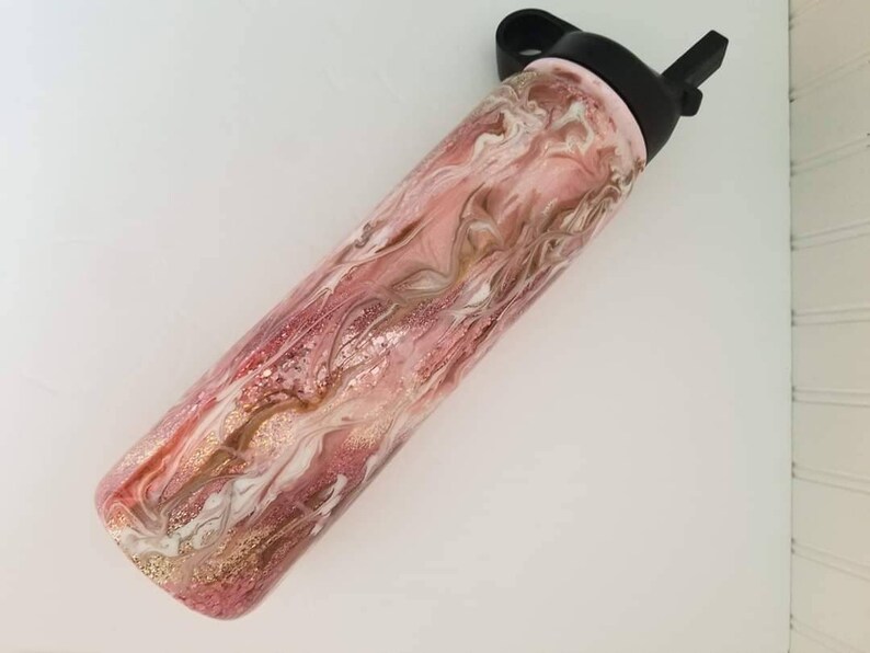 May include: A pink and gold water bottle with a black lid and a straw. The bottle has a marbled design with swirls of pink, gold, and white.