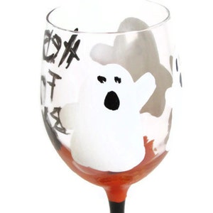 May include: A clear glass wine glass with a black and white ghost design and orange paint around the base. The glass has the words "Boo!" written on it.