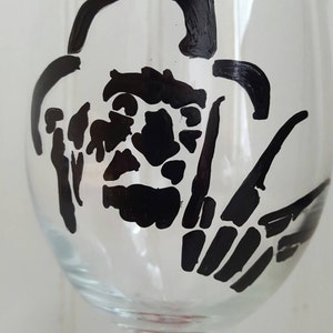 Pu&ograve; includere: Un bicchiere da vino in vetro trasparente con una silhouette nera del viso e della mano di un personaggio di un film horror. Il gambo del bicchiere &egrave; dipinto con strisce rosse.