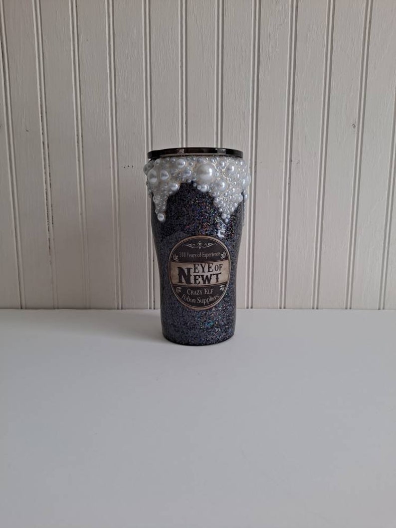 May include: A black glitter tumbler with a white pearl rim and a label that reads "11 Years of Experience Eye of Newt Crazy Elf Potion Supplies".