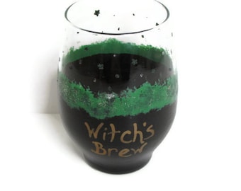 May include: A black glass with a green and black design. The glass has the words "Witch's Brew" written on it in gold paint.