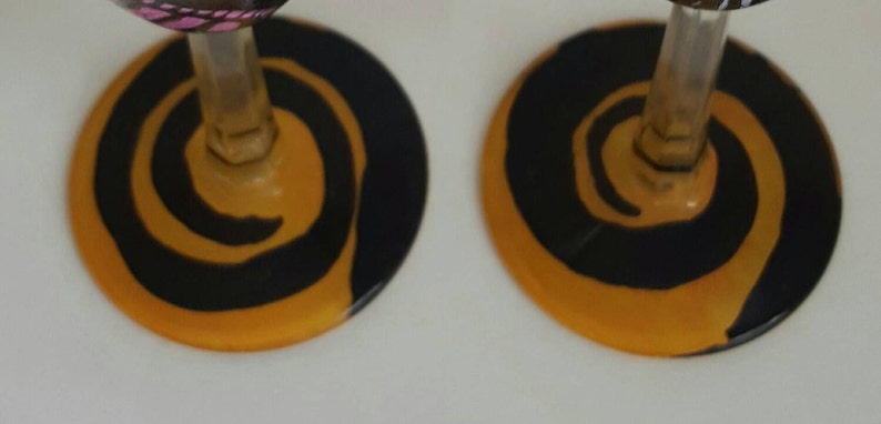 Pode incluir: Duas ta&ccedil;as de vinho com desenhos de espiral preto e laranja na base do copo.