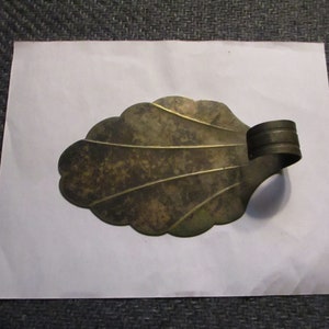 May include: A vintage brass leaf-shaped doorstop with a decorative handle. The doorstop has a worn, aged patina.