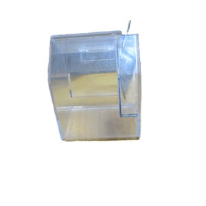 May include: A clear, rectangular plastic container with a small, rectangular opening on the side. The container has a slightly angled design and a small metal piece attached to the top.