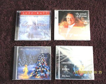 May include: Four music CDs in clear plastic cases. Top left: Jeff Ball Songs of Winter with a snowy teepee. Top right: The Miracle of Christmas with a man's portrait. Bottom left: Trans-Siberian Orchestra with a Christmas tree. Bottom right: Christmas at the Mission by Roben Romero.