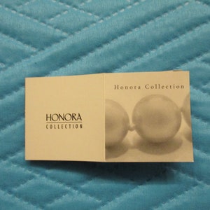 May include: A white card with the text "Honora Collection" printed on it. The card has a picture of a pearl necklace on it.