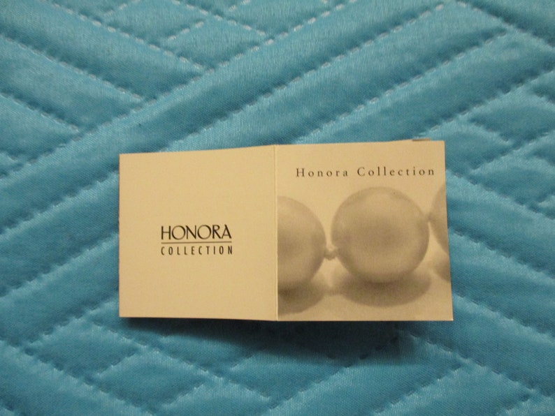 May include: A white card with the text "Honora Collection" printed on it. The card has a picture of a pearl necklace on it.