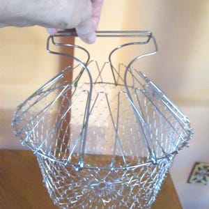 May include: A silver collapsible wire basket with a handle. The basket is made of a fine mesh wire and is designed to be folded flat for storage.