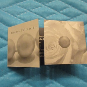 May include: A close-up of a folded card with the text "Honora Collection" on the front. The card features a pearl necklace and a white rose.