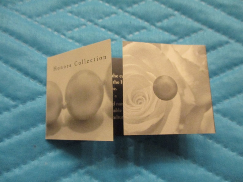 May include: A close-up of a folded card with the text "Honora Collection" on the front. The card features a pearl necklace and a white rose.