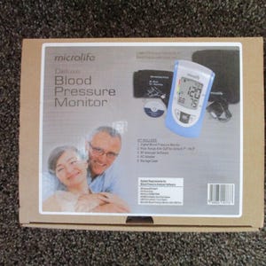 May include: A white box with a blue and white blood pressure monitor on the front. The box says "microlife Deluxe Blood Pressure Monitor".