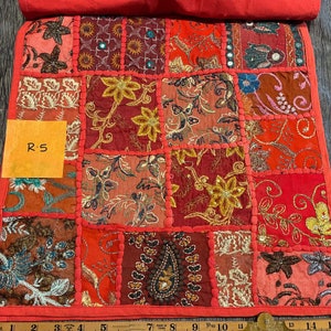 May include: A patchwork textile with a vibrant mix of red, orange, and gold fabrics. The design features embroidered floral patterns and mirrored accents. The textile has a red border and a tag that reads "R-5".