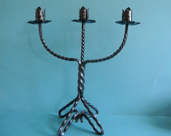 May include: A black metal candelabra with three candle holders. The candelabra has a twisted design and a wide base.