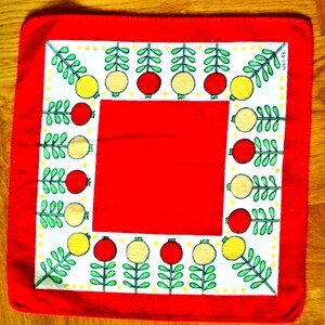 May include: A square red cloth with a white border featuring a repeating pattern of stylized red and yellow fruit with green leaves. The center of the cloth is solid red. The text "ULLAS" is visible in the corner.