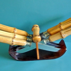 May include: A set of six steak knives with bamboo handles and a dark brown plastic stand. The knives have stainless steel blades and the handles are a light brown colour.