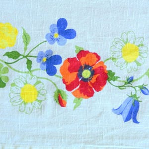 May include: A white tablecloth with a floral pattern featuring red, yellow, blue, and green flowers. The flowers are stylized and have a vintage look.