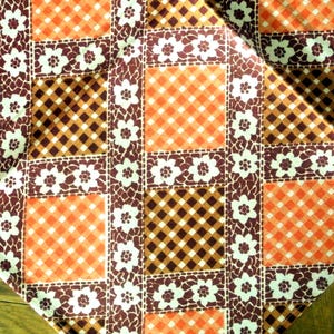 May include: A fabric textile featuring a repeating grid pattern of alternating orange and dark brown gingham squares, separated by vertical and horizontal bands of dark brown fabric decorated with a white five-petalled floral print.