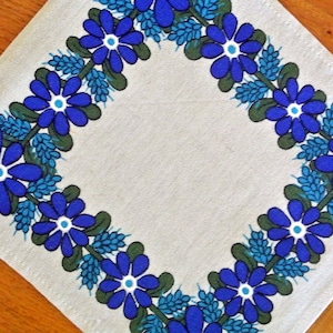 Könnte beinhalten: Ein weißer Leinen-Platzteller mit einem blauen und grünen floralen Rand. Der Rand zeigt ein sich wiederholendes Muster aus stilisierten blauen Blumen mit weißen Zentren und grünen Blättern.
