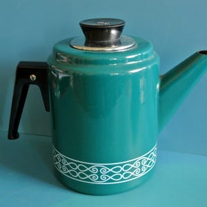 以下が含まれることがあります： ターコイズブルーのエナメル製のコーヒーポット。底に白い装飾バンドが付いています。ポットには黒いハンドルと黒い蓋が付いています。
