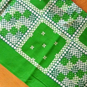 Op de afbeelding: Groene stof met een wit en groen geometrisch patroon. Het patroon heeft kleine witte stippen, vierkanten en klavertjesvier.
