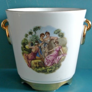 Może przedstawiać: Biała doniczka ceramiczna ze złotymi uchwytami i malowanym obrazem czterech kobiet w ogrodzie.