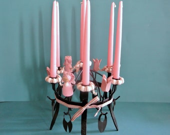 May include: A black metal candelabra with six pink candles and pink fabric dolls around the base. The candelabra is decorated with a white and pink ribbon.