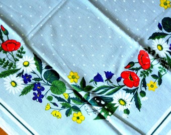 May include: A light blue tablecloth with a white polka dot pattern and a floral border. The border features red poppies, white daisies, yellow flowers, and blue bellflowers. The tablecloth has a white and green striped border.