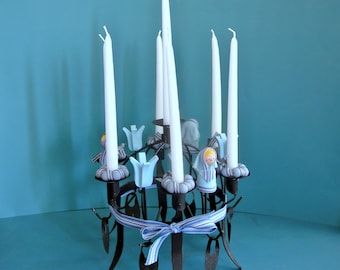 May include: A black metal candelabra with six white candles and blue and white decorations. The candelabra is decorated with small blue and white figurines.