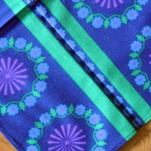 May include: Blue fabric with a green and white striped pattern. The fabric has a repeating design of purple and blue flowers with green leaves.