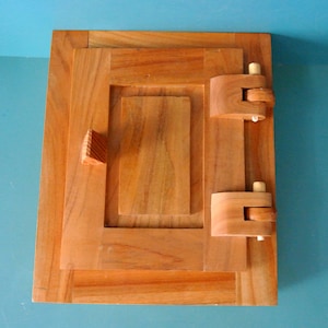 May include: A wooden box with a hinged lid and two wooden latches. The box is made of light brown wood and has a natural finish.