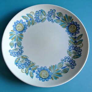 May include: A white ceramic plate with a blue and green floral design. The plate has a circular shape and a raised rim.
