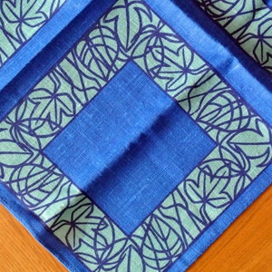 May include: A blue linen tea towel with a green and white leaf pattern border.