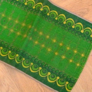 May include: A green and yellow patterned rug with a repeating design of circles and swirls. The rug is made of a woven fabric and has a fringed edge.
