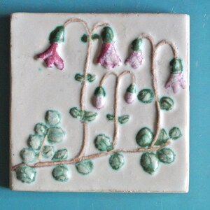 May include: Square ceramic tile with a raised floral design. The off-white tile features a brown stem with green leaves and pink and purple bell-shaped flowers. The tile is likely for decorative use.