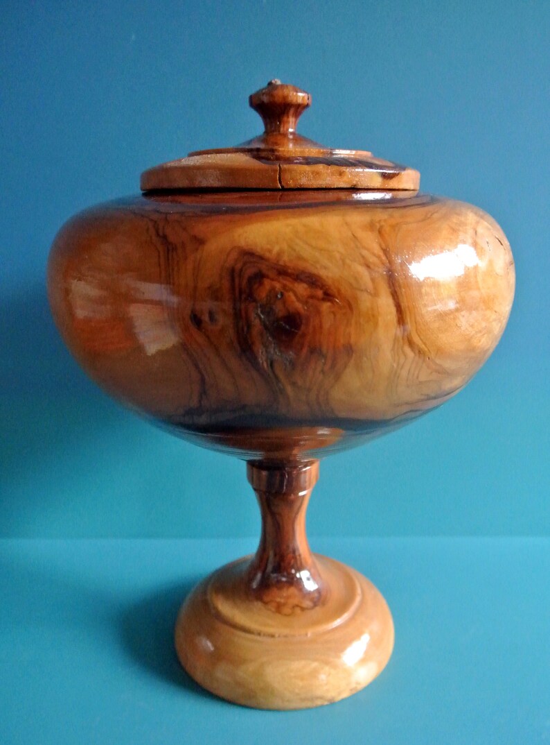 May include: A wooden bowl with a lid, on a pedestal base. The bowl is made of a dark wood with a natural grain pattern. The lid has a small knob on top.