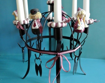 Puede incluir: Un candelabro de metal negro con seis portavelas y una cinta rosa. El candelabro está decorado con pequeñas figuras de madera de personas vestidas con ropa tradicional.