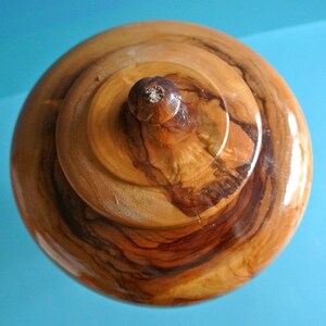 May include: A wooden lidded box with a natural wood finish. The lid has a knob on top and the wood grain is visible.