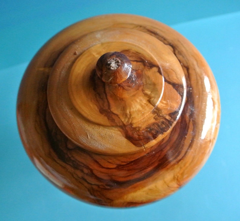 May include: A wooden lidded box with a natural wood finish. The lid has a knob on top and the wood grain is visible.