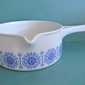 May include: White ceramic saucepan with a blue snowflake pattern around the rim. The saucepan has a single handle.