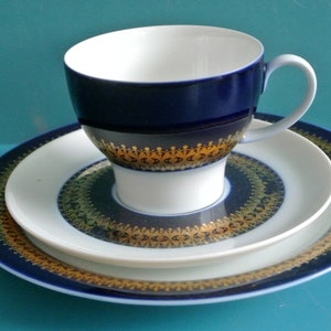 Puede incluir: Un juego de taza y platillo de té azul y dorado. La taza y el platillo tienen un borde dorado con un patrón repetitivo. La taza está sobre el platillo.