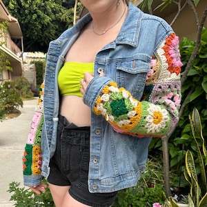 May include: A denim jacket with crocheted sleeves. The sleeves are made of colorful squares in shades of pink, green, yellow, and orange.