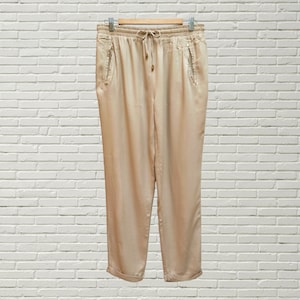 Puede incluir: Pantalón beige con cintura de cordón y bolsillos laterales. El pantalón tiene un corte holgado y está hecho de una tela suave y ligera.
