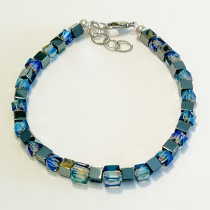 May include: A silver bracelet with dark grey and iridescent blue square beads.