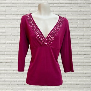 Peut inclure: Un haut à manches longues de couleur bordeaux avec un décolleté en V profond. Le décolleté est orné d'un motif de paillettes argentées.