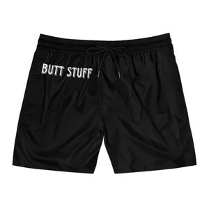 May include: Black shorts with an elastic waistband and drawstring. The shorts feature the white text "BUTT STUFF" across the front. These shorts are suitable for casual wear or water activities.