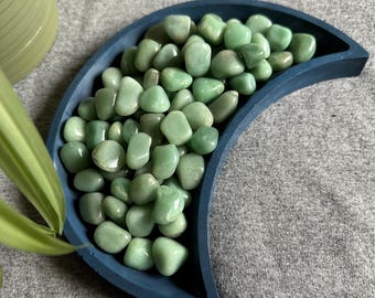 May include: A blue crescent moon-shaped dish filled with smooth, light green tumbled stones.