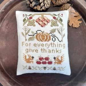 May include: A white cushion with a cross-stitch design featuring a pumpkin, leaves, and the text "For everything give thanks".